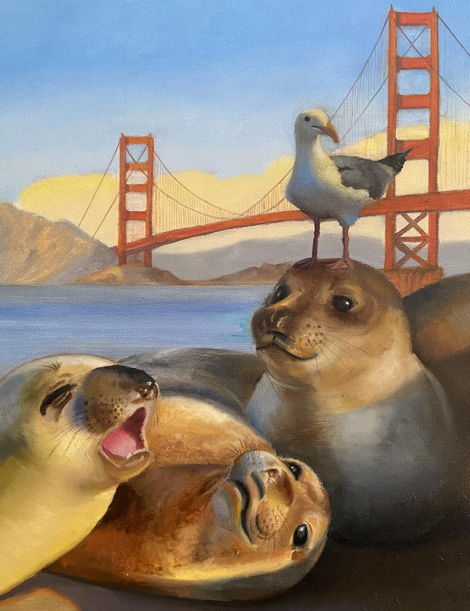Three seals rest on the shore in front of the Golden Gate Bridge. A gull stands on one of the seal's heads.