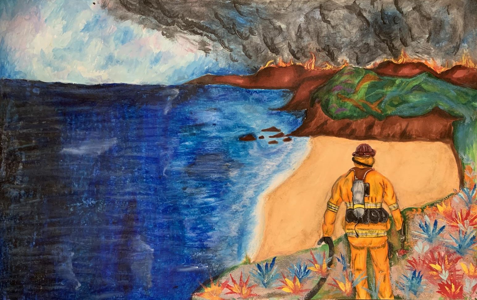 a firefighter stands looking out at the coast. in the distance flames and smoke rise above the bluffs