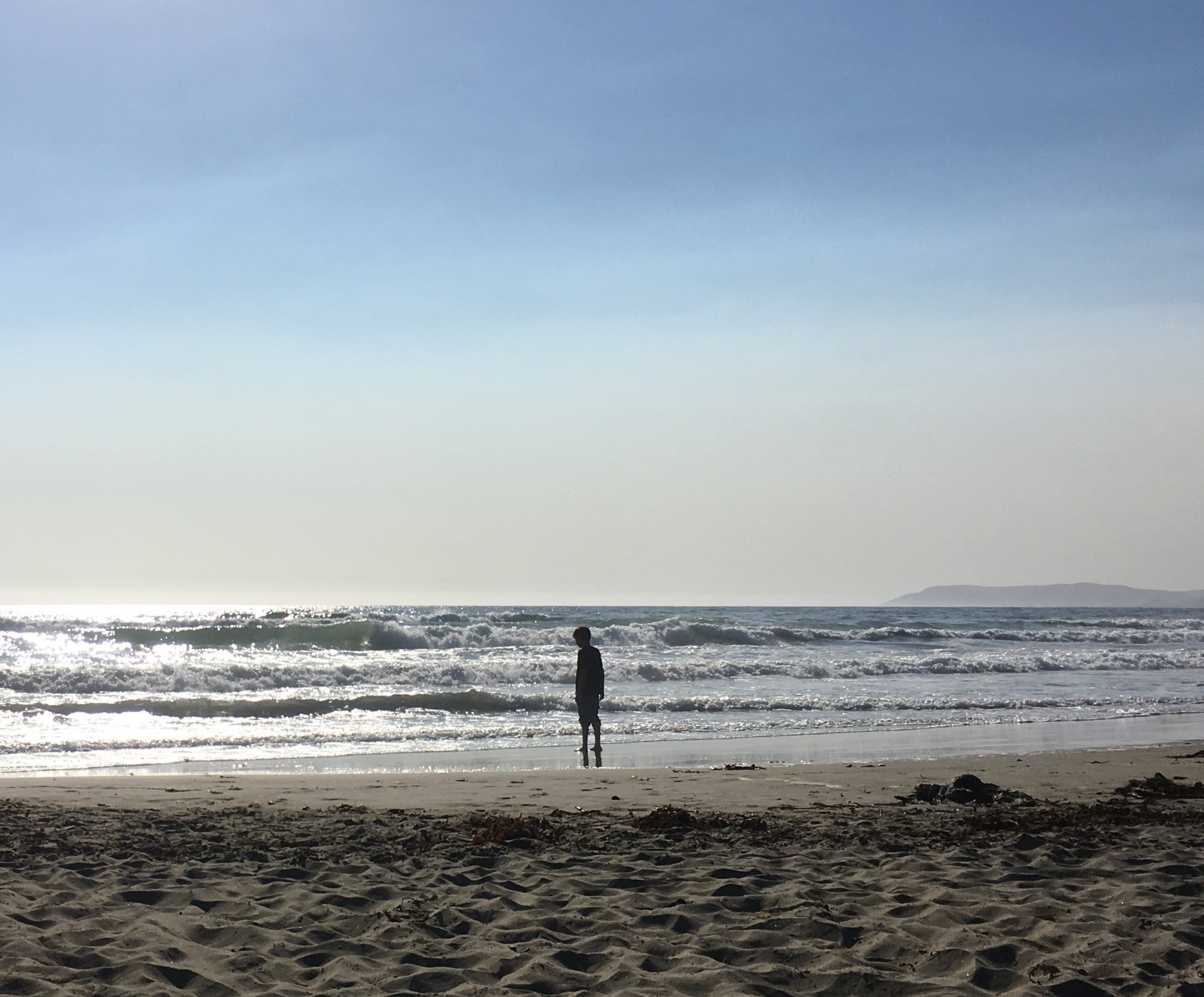 A child stands on the beach looking out at the waves