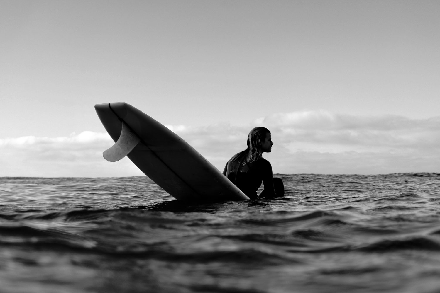 A surfer sits on a surfboard, looking off towards the waves.