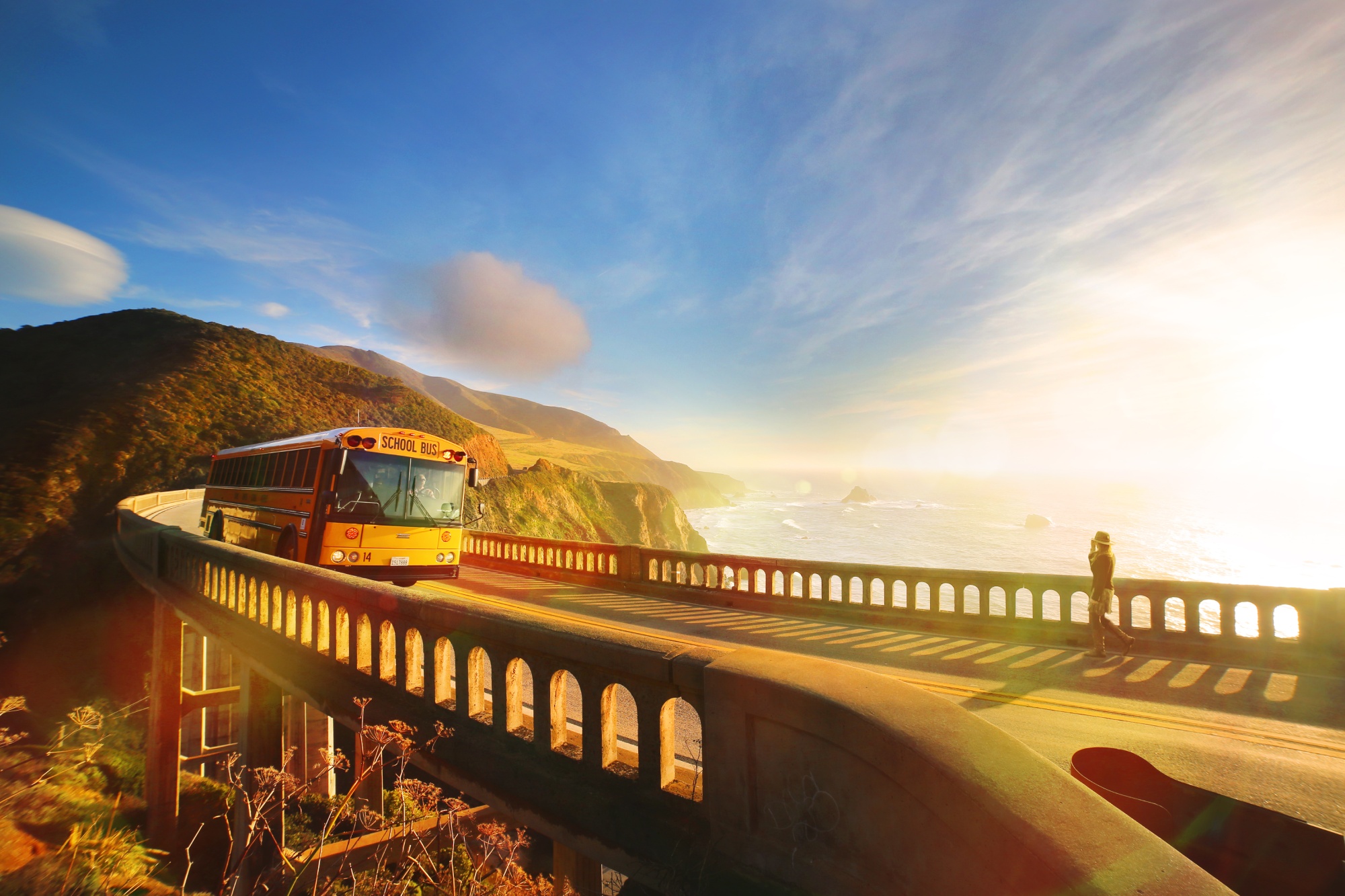 a school bus drives across the bridge toward the viewer on a sunny day