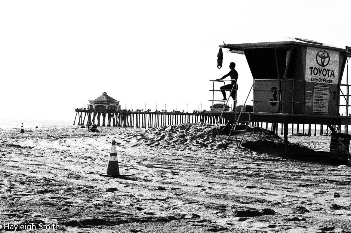 A lifeguard sitting on a lifeguard tower looks out at the ocean