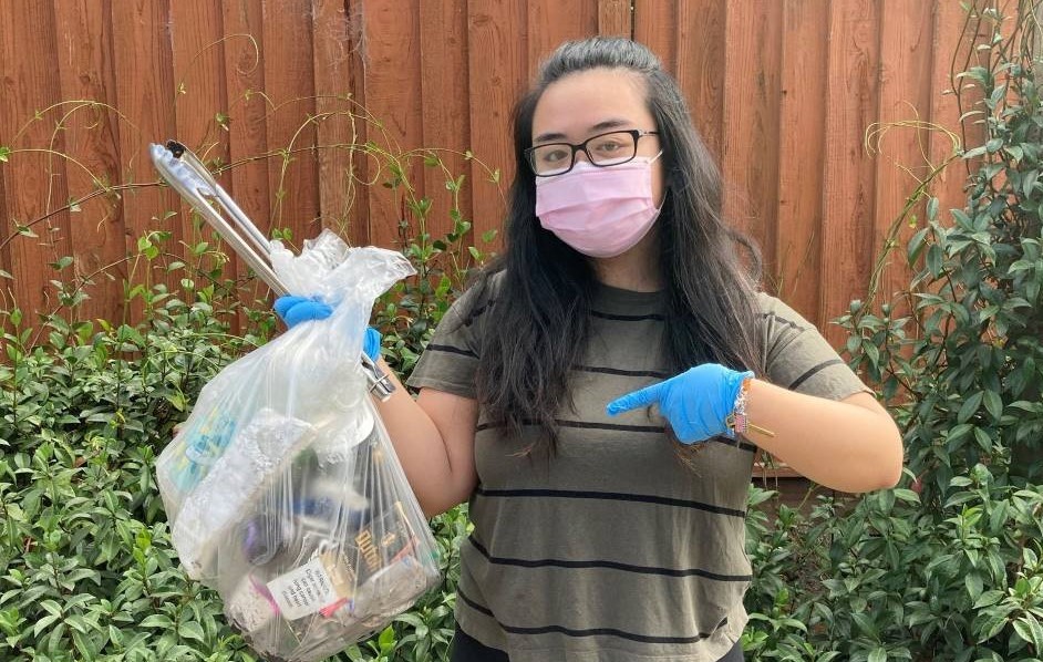 A masked woman on a sidewalk holding a full bag of trash