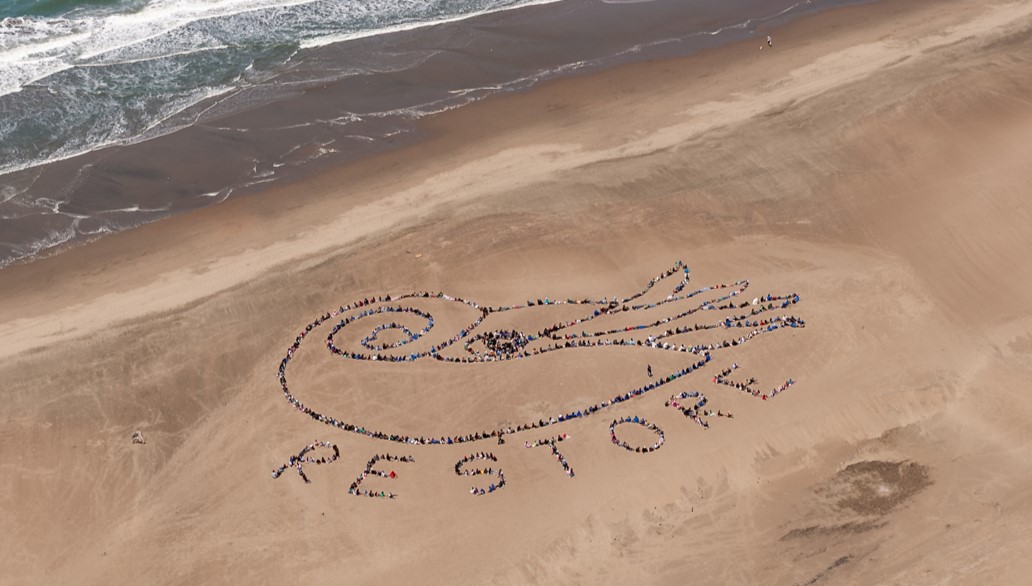 San Francisco Kids' Ocean Day aerial artwork. People on the sand form an image of a nautilus, with the word Restore.