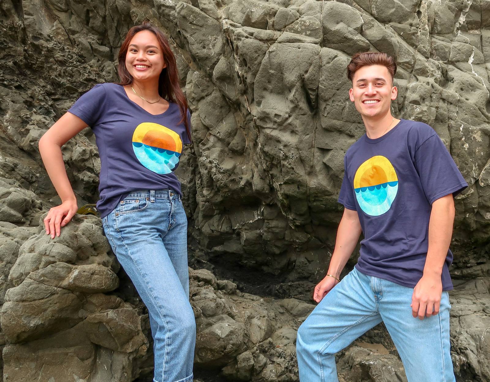 Two smiling people wearing the 2023 Coastal Cleanup Day Shirt with round image of sun setting on the ocean