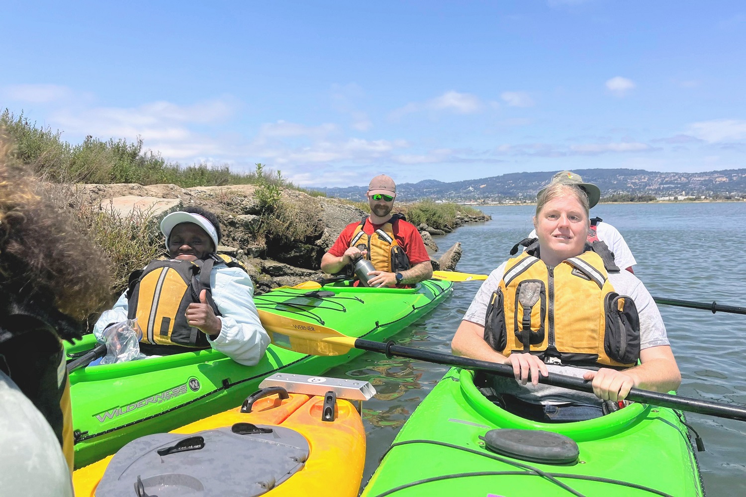 Kayakers of different abilities take a break from paddling, smiling and give a thumbs up