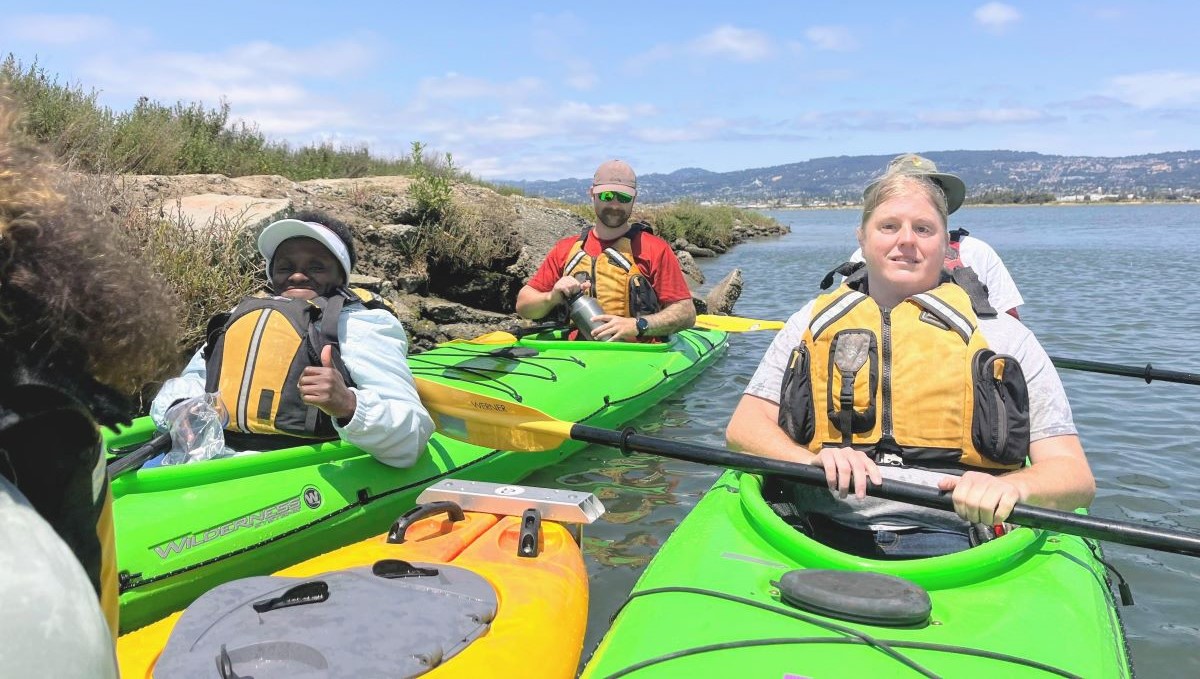 People in kayaks and life jackets smile for the camera